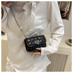 Close-up of black quilted mini bag featuring large pearl handle and silver metal turn-lock