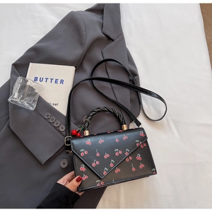 Détail du sac bandoulière noir à motif cerises avec rabat en V et breloque cerise