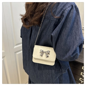 Detail of cream white mini crossbody bag with silver bow and metal chain strap