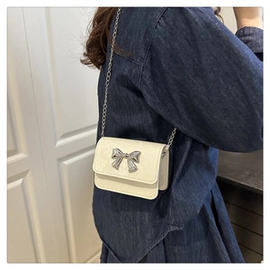 Detailed view of a white crossbody bag featuring a silver bow buckle and metal chain strap