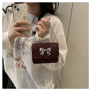 Mini burgundy crossbody bag with snake-pattern leather and silver bow detail worn by model