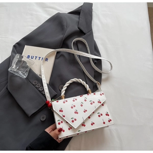 Détail du petit sac carré à imprimé cerise avec poignée tressée sur un blazer gris