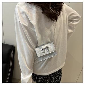 Detail of silver snake-pattern mini crossbody bag with silver bow accent on model