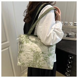Detail of canvas tote bag featuring green bamboo prints and wide woven straps on model