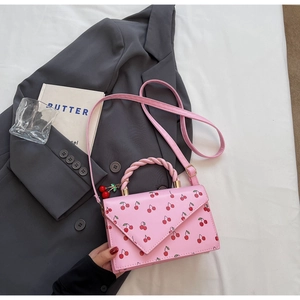 Détail du sac à main rose à motif cerises avec poignée tissée et pendentif cerise rouge