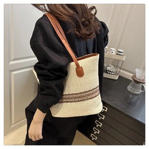 Detail of a large woven tote bag with brown leather straps and geometric pattern accents