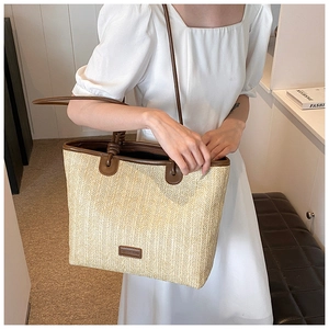Detailed view of the woven straw shoulder bag with brown leather trim and shoulder strap