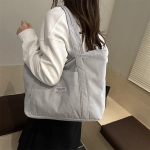 Light blue corduroy tote bag with fashion label shown in a stylish shoulder carry pose