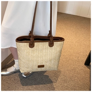 Detail of hand-woven straw tote bag featuring brown leather handles and knot accents