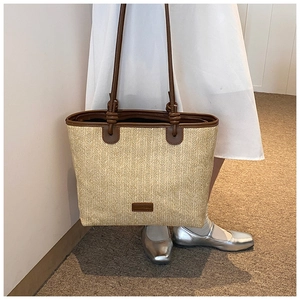 Detail of hand-woven straw tote bag featuring brown leather handles and brand tag