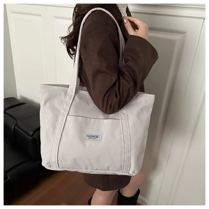 Detail of off-white corduroy tote bag showing vertical texture and fashion label