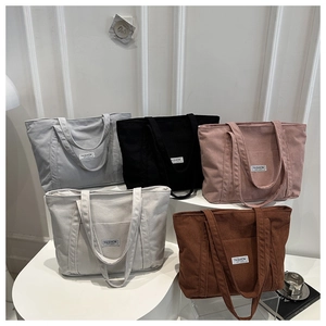 Stack of corduroy tote bags in grey black pink beige and caramel showing front pocket details