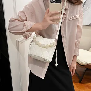 Sac seau matelassé blanc avec poignée en perles et bandoulière porté par le modèle