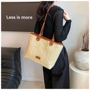 Detail of hand-woven straw tote bag with brown leather straps shown on a model