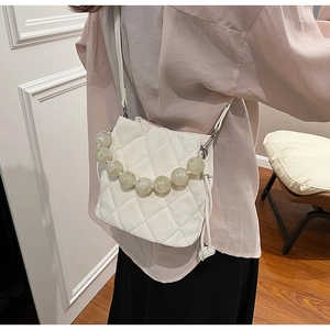 Sac bandoulière matelassé avec chaîne de perles porté par un mannequin en intérieur
