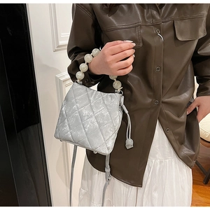 Détail d'un sac seau matelassé argenté avec poignée en perles et fermeture à cordon pratique