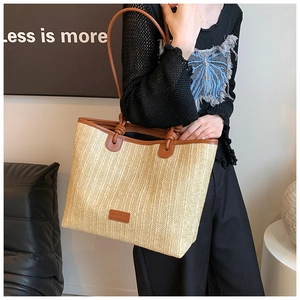 Detail view of woven straw tote bag featuring brown leather trim and knotted shoulder strap