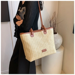 Detail of hand-woven straw tote bag featuring leather straps and decorative knot accents