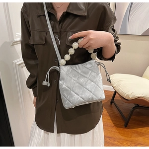 Détail d'un sac seau matelassé argenté avec poignée en perles et fermeture à cordon