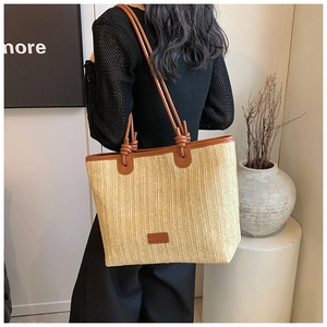 Detail of a large straw tote bag with brown leather trim and knot handle on a model