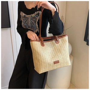 Detail of hand-woven straw tote bag with brown leather knotted straps and brand label