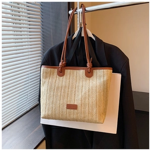 Close-up of woven straw tote bag featuring brown leather knotted handles and trim