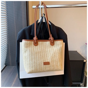 Detail of woven straw tote bag with brown leather shoulder straps and branded patch