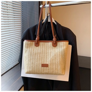 Detail of woven straw tote bag featuring brown leather handles with knot accents
