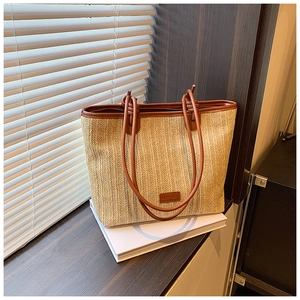 Detail view of woven straw tote bag with brown leather handles and decorative patch