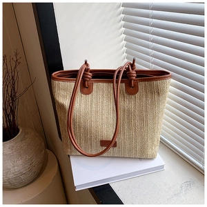 Detail of woven straw tote bag with brown leather handles and knot accents on white books