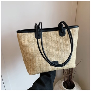 Detail of woven straw tote bag with black leather handles and rectangle logo patch