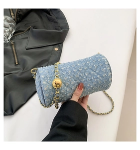 Détail du sac cylindre en denim bleu clair avec paillettes, chaîne dorée et boule réglable