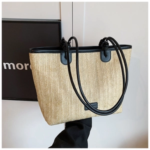 Detail of straw woven tote bag featuring black leather trim and elegant knotted shoulder strap