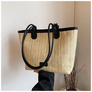 Detail showing woven paper straw texture and black leather handles of a summer tote bag