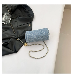 Détail du sac cylindrique à paillettes bleues avec chaîne dorée sur fond urbain
