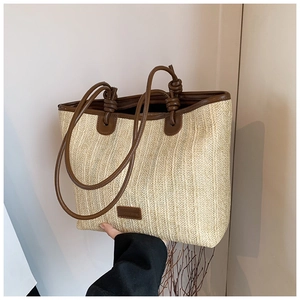 Detail of woven straw tote bag featuring leather handles and a decorative front patch