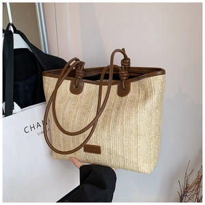 Detail of woven straw tote bag with brown leather knotted handle and logo patch