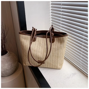 Detail of woven straw tote bag with brown leather trim and handles by a sunny window