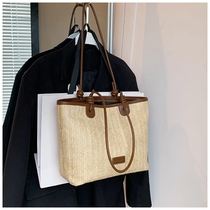 Detail of woven straw tote bag with brown leather handles and brand logo patch