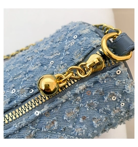 Détail du tissu denim bleu clair avec paillettes argentées et fermeture éclair dorée