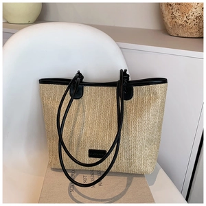 Detail of woven straw tote bag featuring black leather trim and long shoulder handles