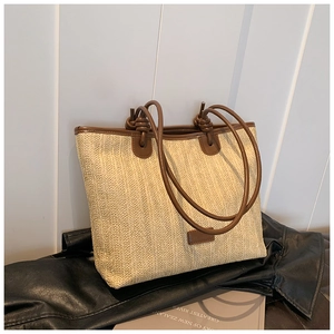 Detail of woven straw tote bag with brown leather trim and knot shoulder strap