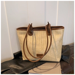 Close-up of beige straw woven tote with brown leather handles and a logo patch