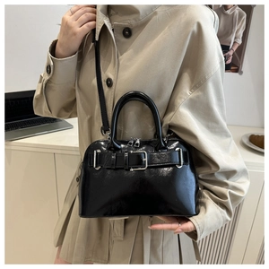 Glossy black shell bag with buckle detail styled on model wearing a beige trench coat