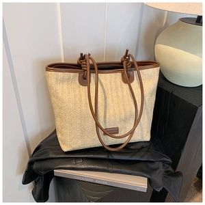 Detail of beige woven tote bag with brown leather handles and logo patch accents