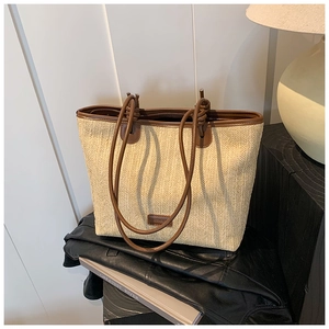 Detail of woven straw tote bag with brown leather handles and logo patch on black leather