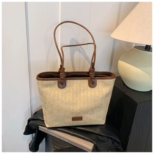Detail of hand-woven straw tote bag featuring brown leather handles and brand patch
