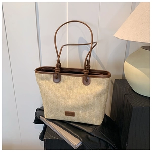 Detail of woven straw tote bag with brown leather trim on a minimalist display stand