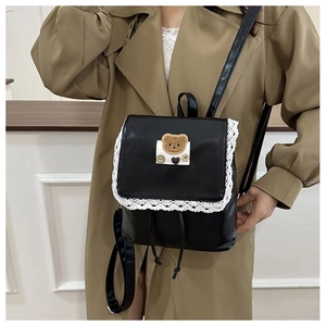 Close-up of black PU mini backpack featuring white lace trim and plush bear patch