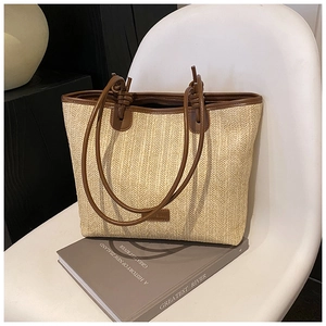 Detail view of woven straw tote bag with brown leather shoulder straps on a chair